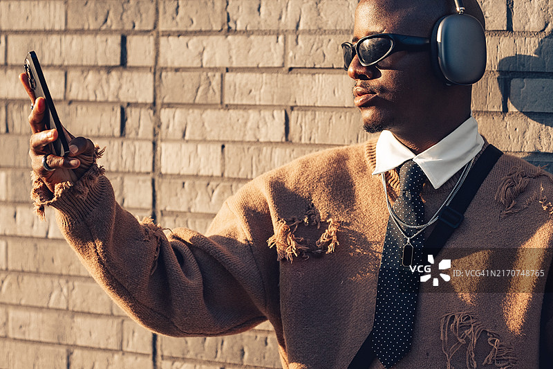 户外系领带的黑人男性肖像。男人身穿棕色毛衣，戴着太阳镜用手机图片素材