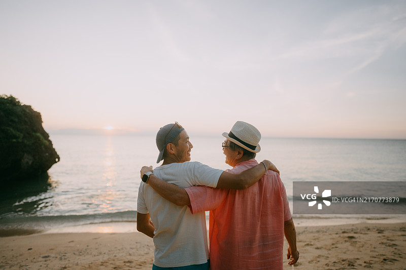 年长的父亲和成年的儿子在日落时分的海滩上图片素材