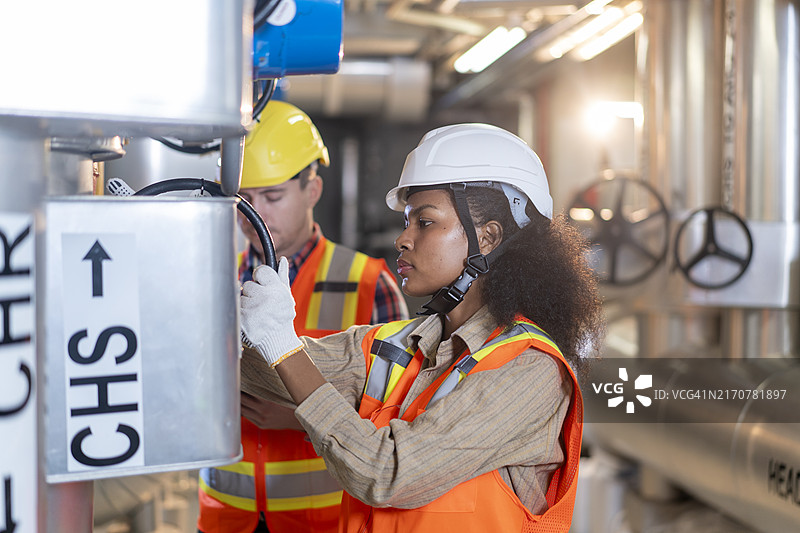 穿着安全设备在煤气管道旁行走并检查分配和消耗的工厂工人图片素材