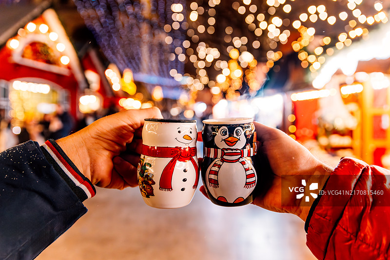 在德国柏林圣诞市场上，两个人从雪人和企鹅形状的杯子里喝热红酒图片素材