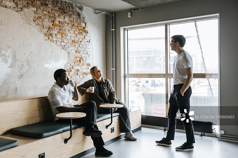 男科技专业人士在办公室与同事喝咖啡交谈图片素材