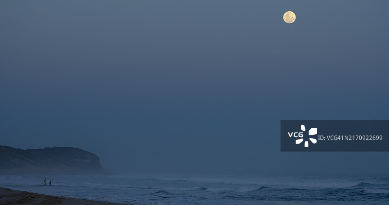 两名冲浪者在澳大利亚维多利亚州十三号海滩的蓝色超级月亮下夜间入海图片素材