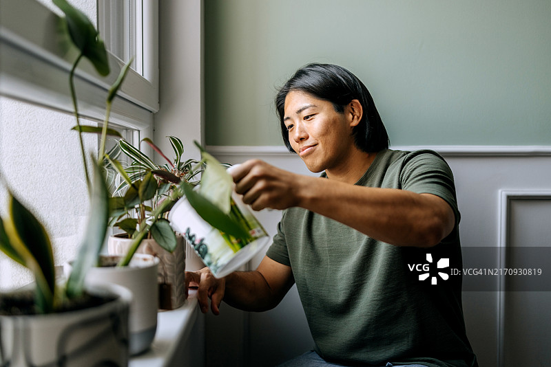 年轻的休闲装男子在家浇花图片素材