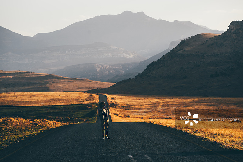公路旅行主题。一名男子沿着通往山脉的空旷道路行走。图片素材