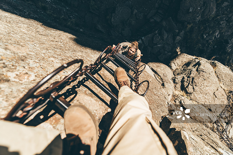 女性攀岩者正在攀爬梯子以到达岩石顶部。图片素材