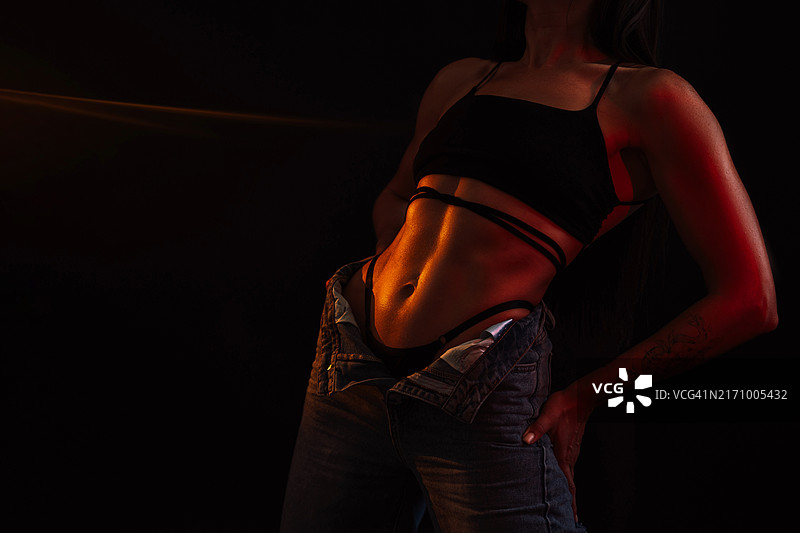 穿着牛仔裤的健康女人在黑色背景上摆姿势图片素材