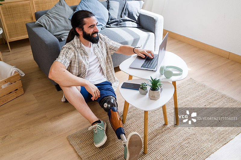 面带微笑的假肢年轻男子在家使用笔记本电脑图片素材