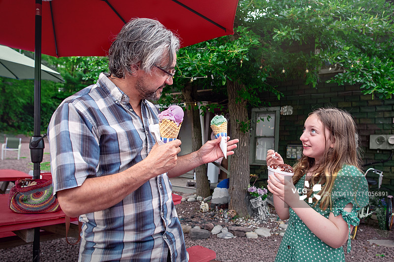 分享甜蜜时刻：53岁父亲和年轻女孩在户外咖啡馆享用冰淇淋图片素材