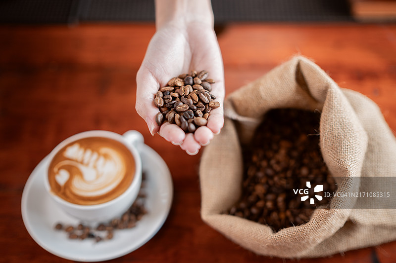 在咖啡店手持新鲜烘焙的咖啡豆和一杯咖啡图片素材