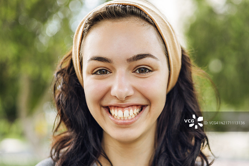 阳光明媚的公园里，戴着发带的卷发年轻女子温暖地微笑图片素材