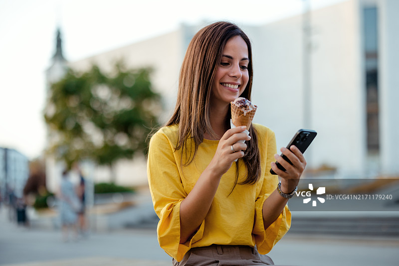 在户外吃冰淇淋和使用智能手机的女人图片素材