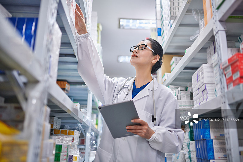 亚洲女药剂师在药房盘点库存的仰视角度图片素材