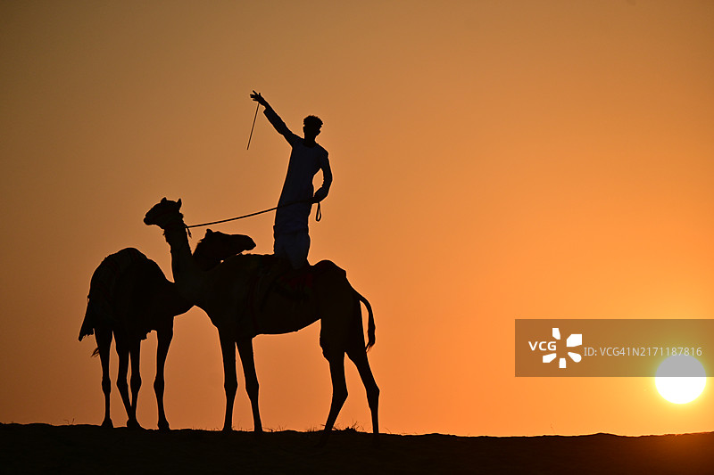 阿联酋迪拜日落时骑着单峰骆驼的男子轮廓图片素材