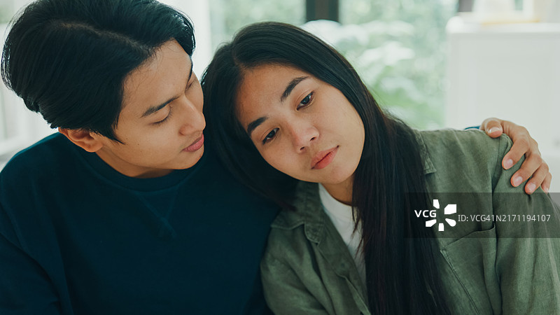 亚洲悲伤男人哭泣，与妻子在家讨论心理健康问题，夫妻之间富有同情心地交流关系问题特写图片素材