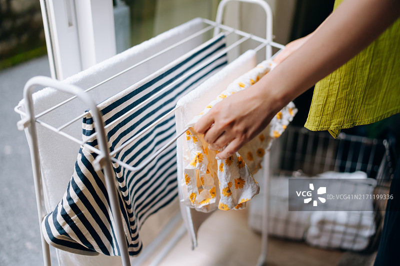 在家洗衣服的年轻女子局部照片。她正在窗边的晾衣架上晾衣服。早晨做家务的女人图片素材