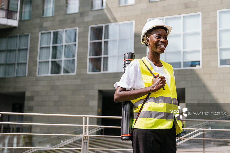 戴着安全帽和工具的快乐非洲女建筑工人在工地上自信地行走图片素材