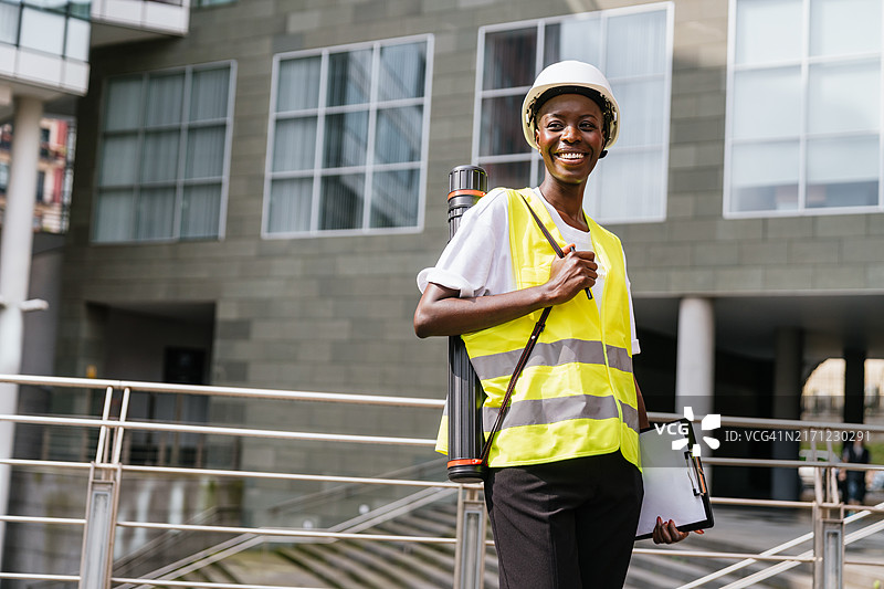 建筑工地上戴着安全帽、穿着背心、携带设备的非洲裔建筑工人图片素材