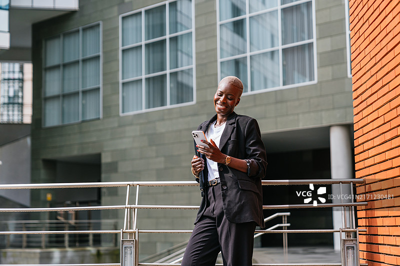 自信的非洲裔女商人站在户外，使用手机，背景是现代建筑图片素材