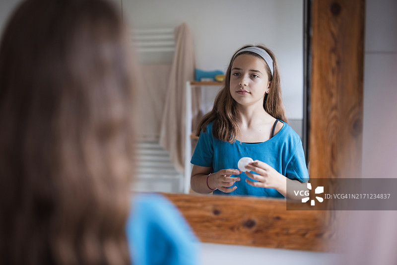 女孩看着镜子中的倒影，手里拿着一片棉垫图片素材