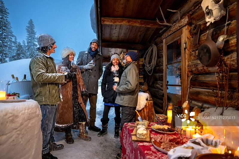 在雪夜小木屋外碰杯的五个不同种族的朋友图片素材