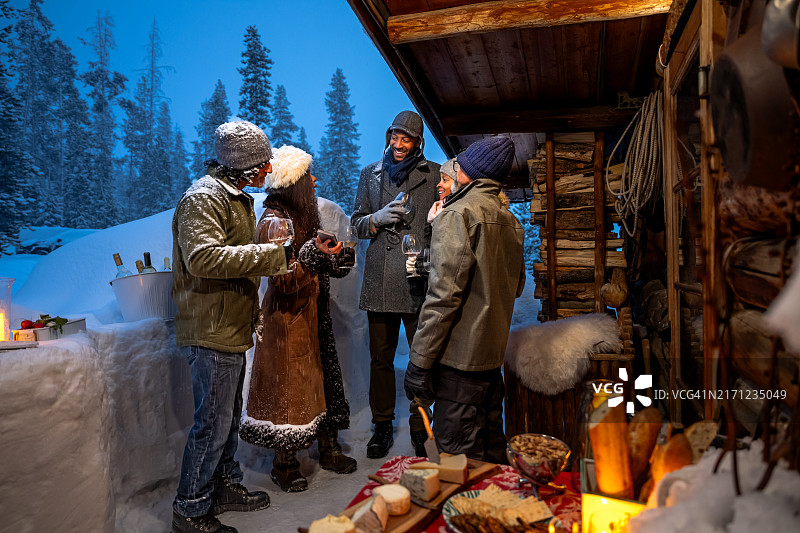 傍晚时分，五个不同种族的朋友在冬季小屋旁游玩图片素材
