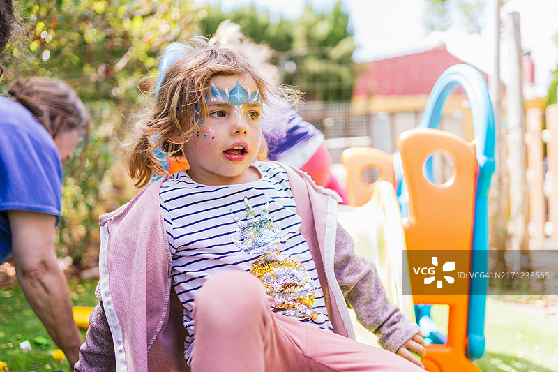 在彩色操场滑梯上玩耍的彩绘脸女孩图片素材