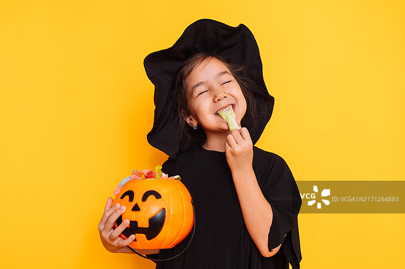 穿着女巫服装，拿着装满糖果的南瓜桶的孩子在吃橘子酱图片素材