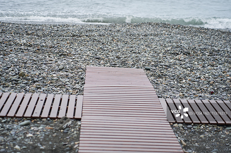 卵石海滩上的木栈道地板。图片素材