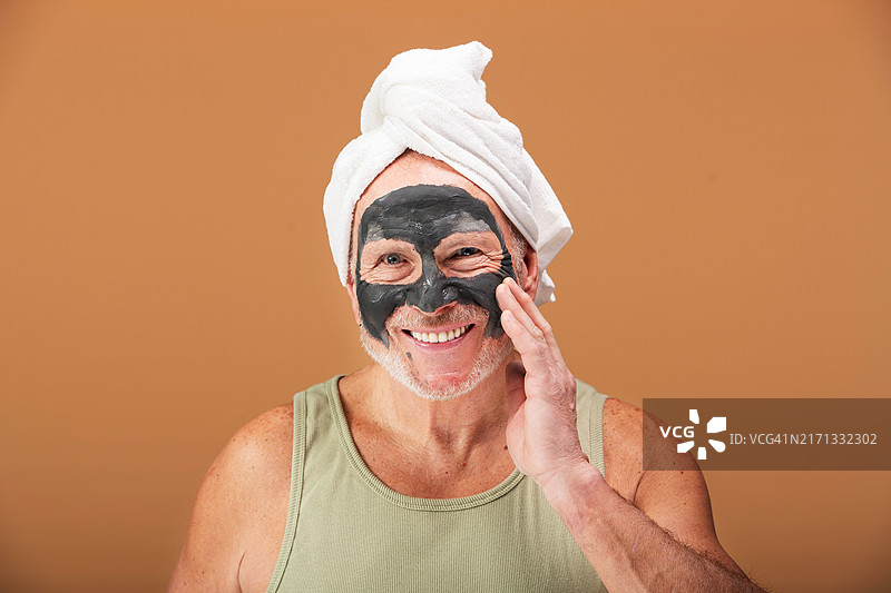 老年男人敷着泥面膜，头顶着毛巾，护理他的肌肤。现代男士的美容和护肤图片素材