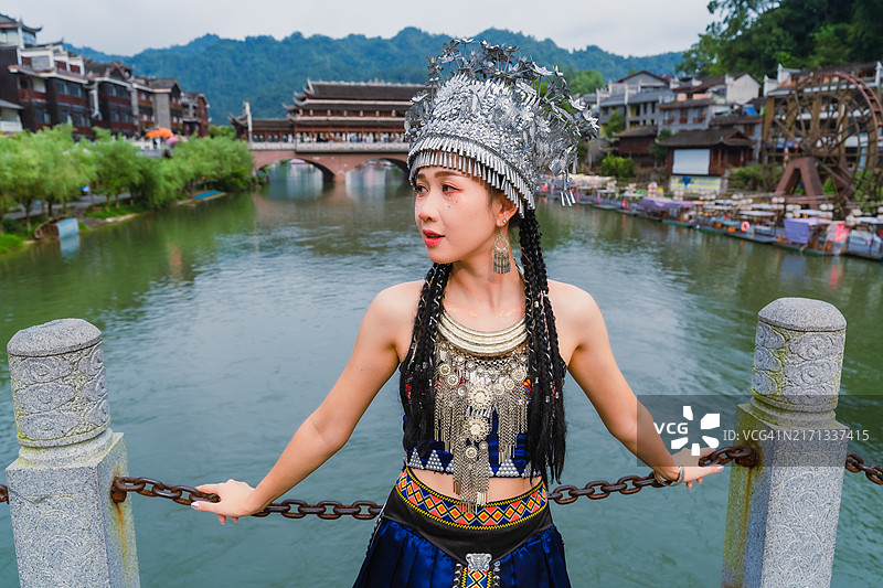 穿着苗族或赫蒙族服饰的中国女游客，仿佛置身于拥有河流和古镇的古城图片素材