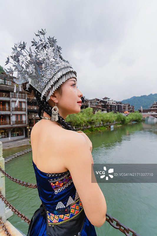 穿着苗族或赫蒙族服饰的中国女游客，仿佛置身于拥有河流和古镇的古城图片素材