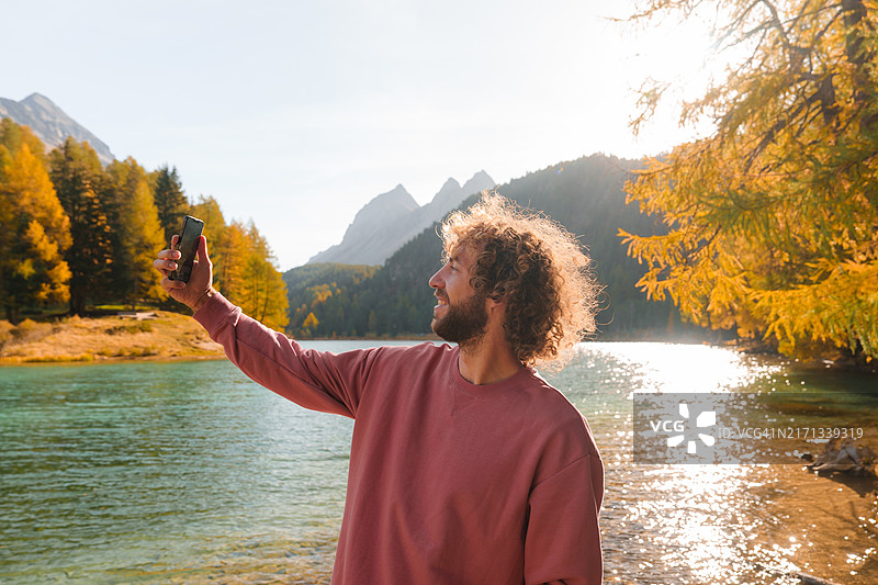 在秋季瑞士阿尔卑斯山湖边使用智能手机的男人图片素材
