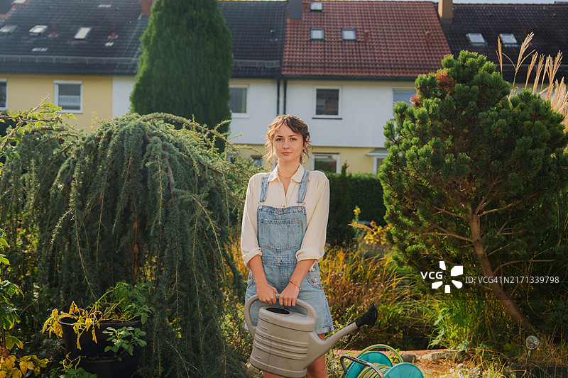 穿着牛仔背带裤在后院浇花的女人图片素材
