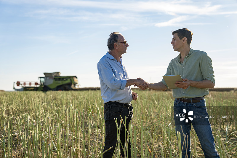 农民在油菜田中与农学家握手，背景是收割机图片素材
