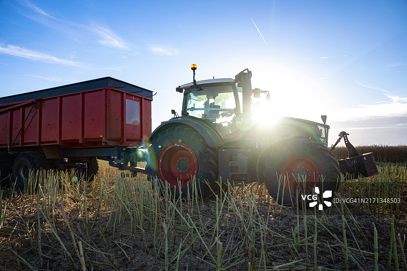 阳光下，耕地里拖拉机拉着拖车剪影图片素材