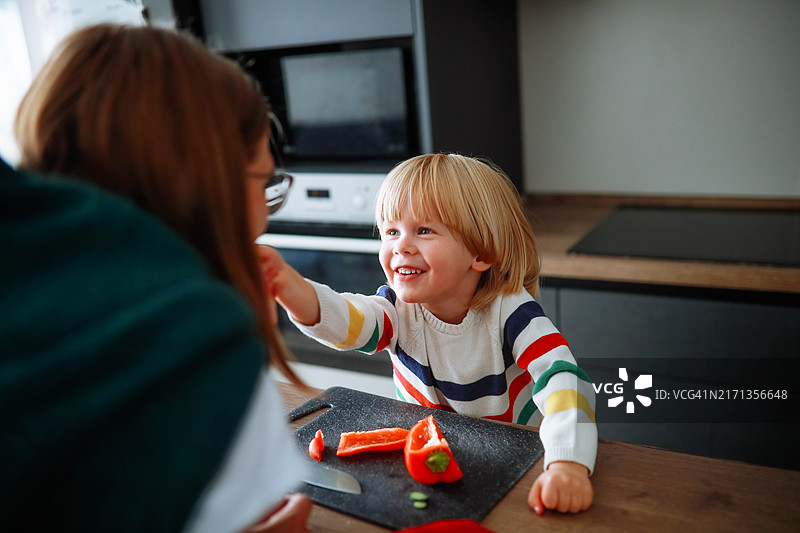 真实的母爱瞬间：怀孕的妈妈和蹒跚学步的儿子准备新鲜沙拉，男孩温柔地给妈妈喂蔬菜，母子情深。图片素材