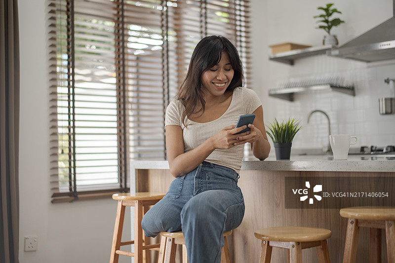 坐在现代厨房里，微笑看着手机的截肢残疾年轻女子图片素材