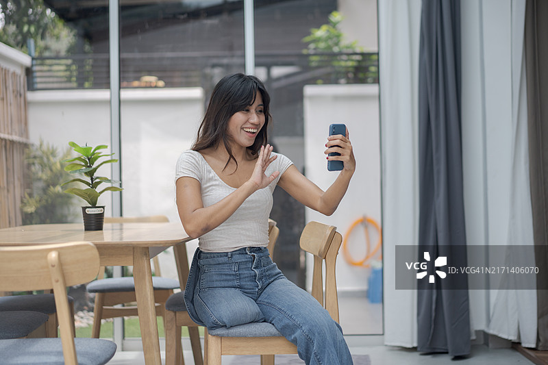 残疾截肢年轻女子坐在现代家居内的木桌旁，用智能手机发短信或浏览互联网图片素材