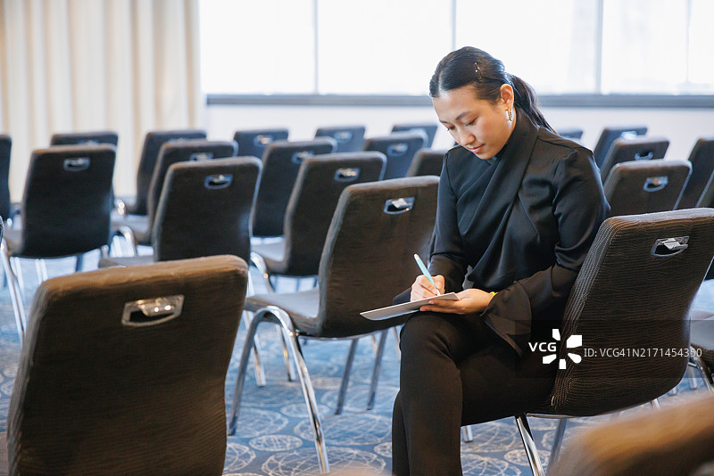 随意坐在椅子上并在笔记本上书写的年轻亚洲女商人肖像图片素材