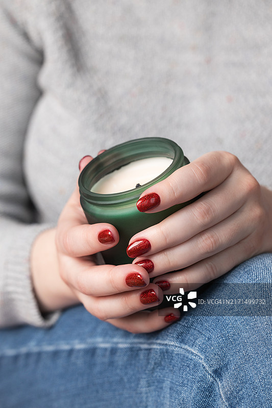 女人手持绿色蜡烛，红色闪光美甲图片素材