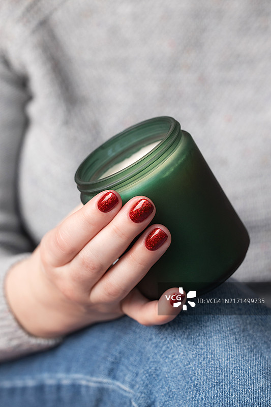 女人手持绿色蜡烛，红色闪光美甲图片素材