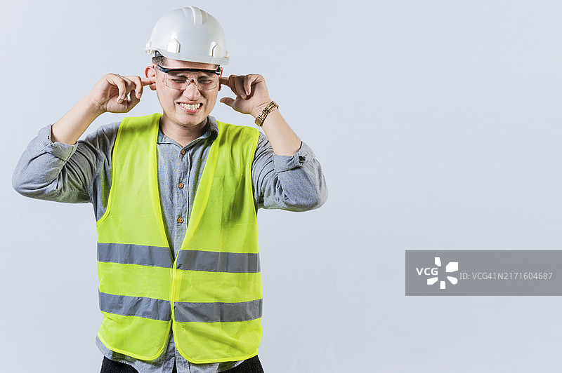 年轻工程师捂住耳朵，与世隔绝。耳朵疼痛的工程师。工程师痛苦地捂住耳朵的概念图片素材