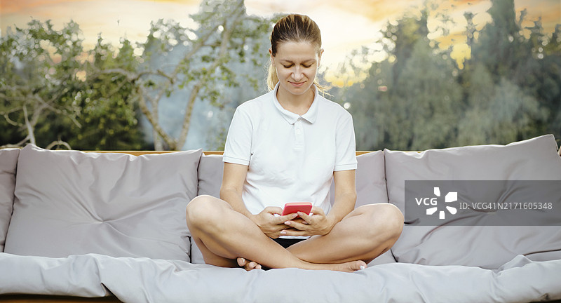 女人在后院舒适的秋千上休息，一边使用智能手机，享受宁静的假期图片素材