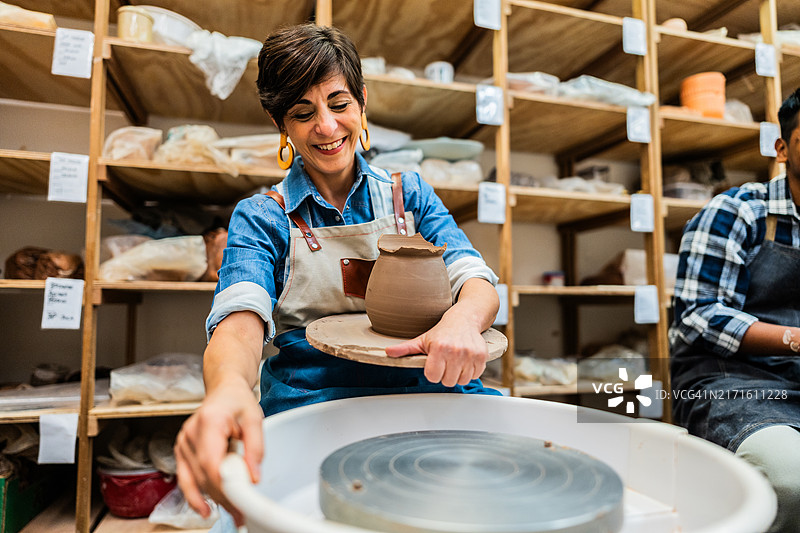 成熟的女性在陶艺工作坊的陶轮上捏制陶土图片素材