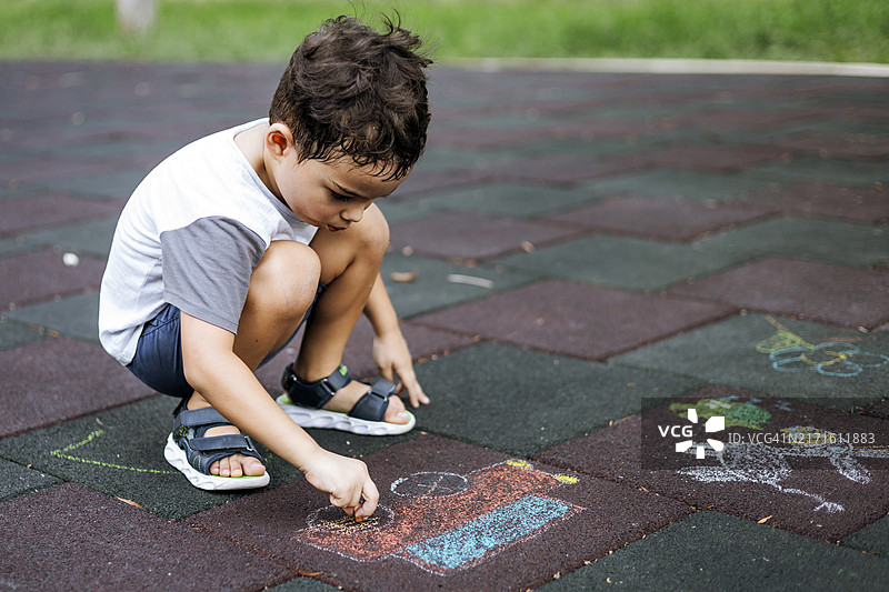 在公园里用粉笔在操场瓷砖上画画的男孩图片素材