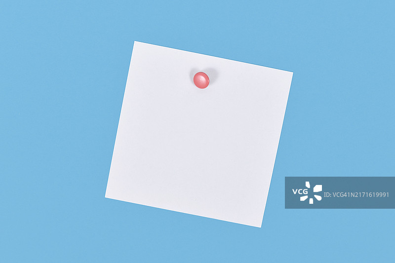 用粉色图钉固定在蓝色墙上的空白白色便签纸图片素材