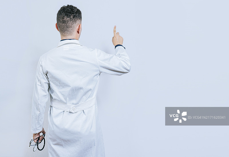 医生指向远方的背影。医生摆姿势，手指指向后方。年轻医生从后面指向远方图片素材