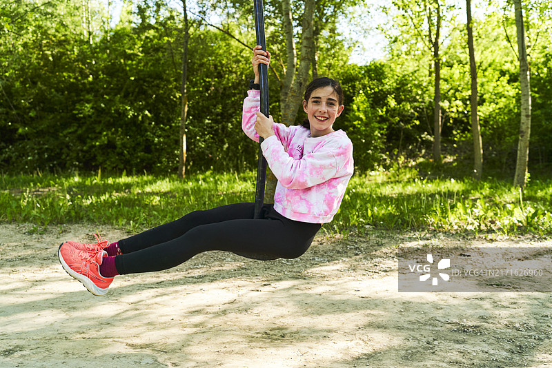 坐在公园秋千上，面带微笑看着镜头的年轻美丽女子侧面肖像图片素材