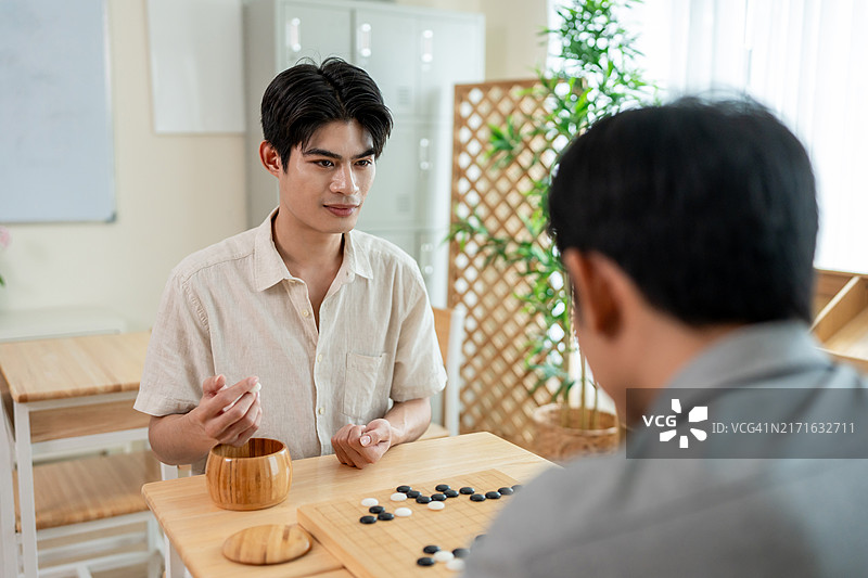 在社区比赛中玩围棋的亚洲青年。两位有魅力的男性朋友参加俱乐部中心桌上的传统亚洲中国棋类比赛。图片素材