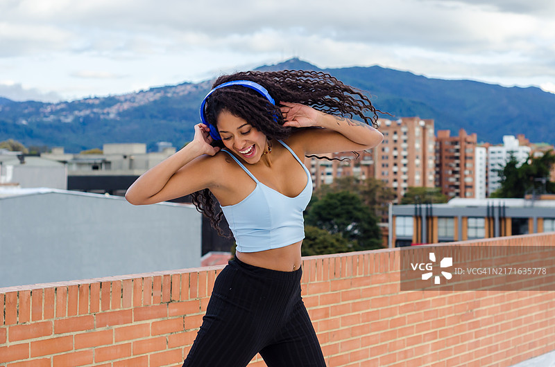 在屋顶跳舞的快乐自信的非裔美国卷发年轻女子和无线耳机图片素材